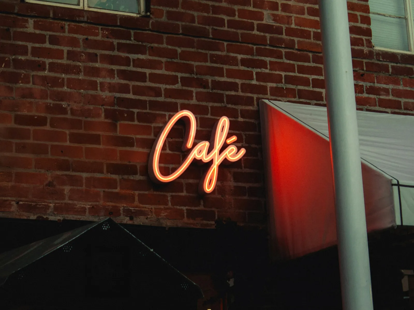 レンガの壁に灯る「Café」のネオン看板と、店先の日よけ